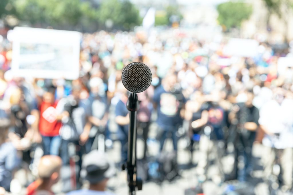 Focus on microphone, blurred group of people at protest in the background