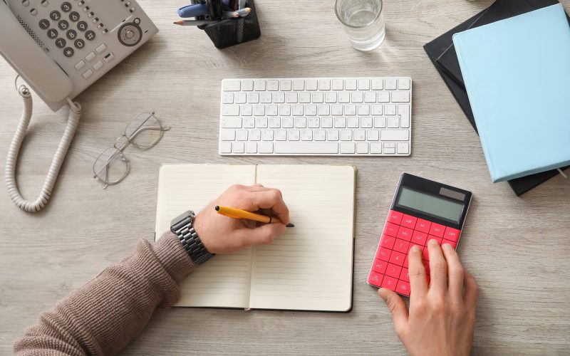 Male hands using calculator and doing notes in office. Top view