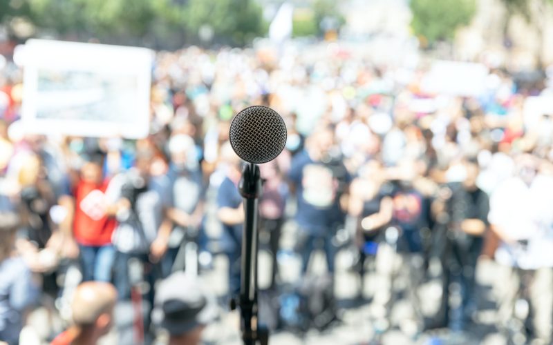 Focus on microphone, blurred group of people at protest in the background